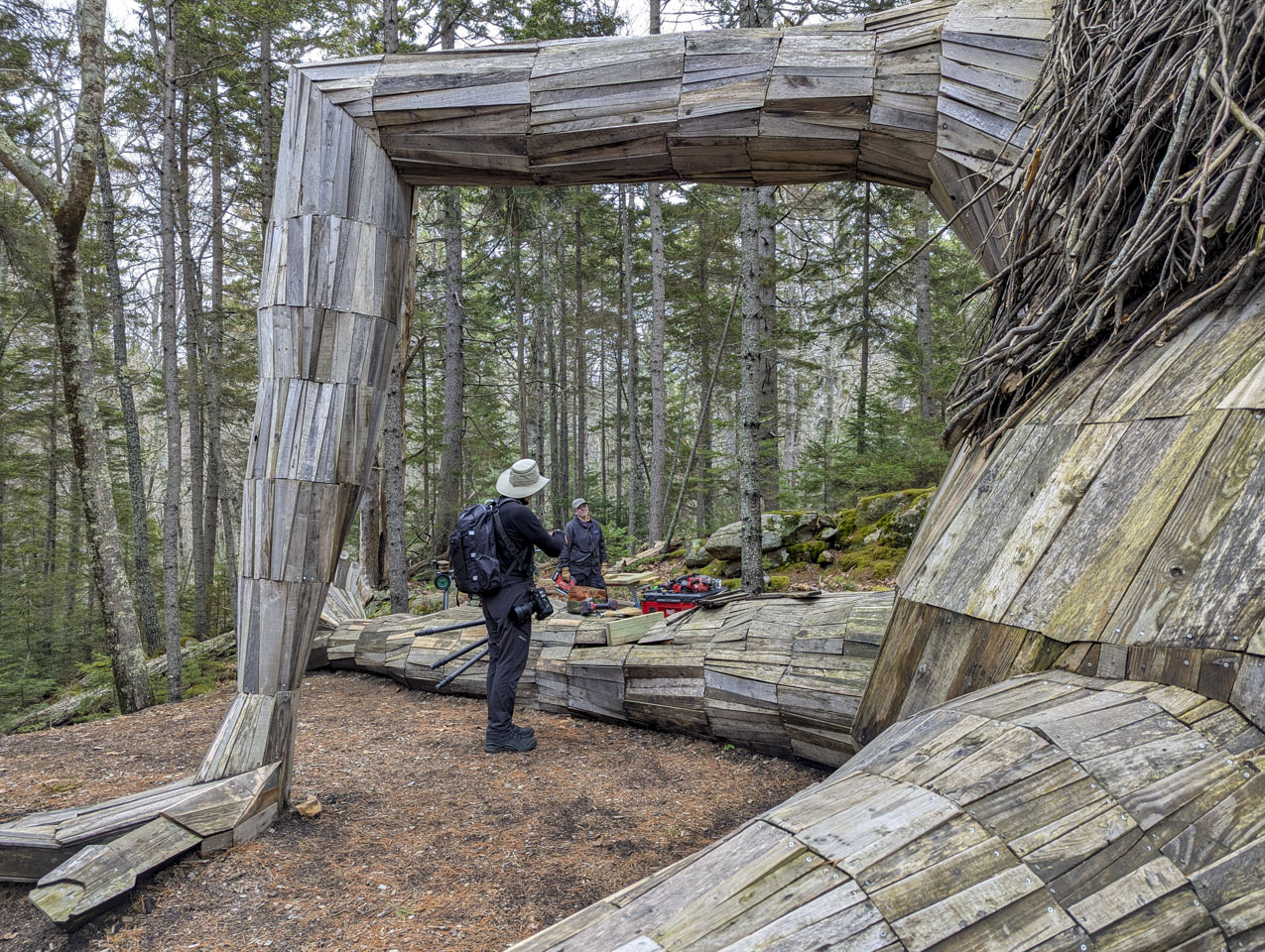 Paul stands under the bent arm of one of the Trolls, talking to a woman holding a power tool.