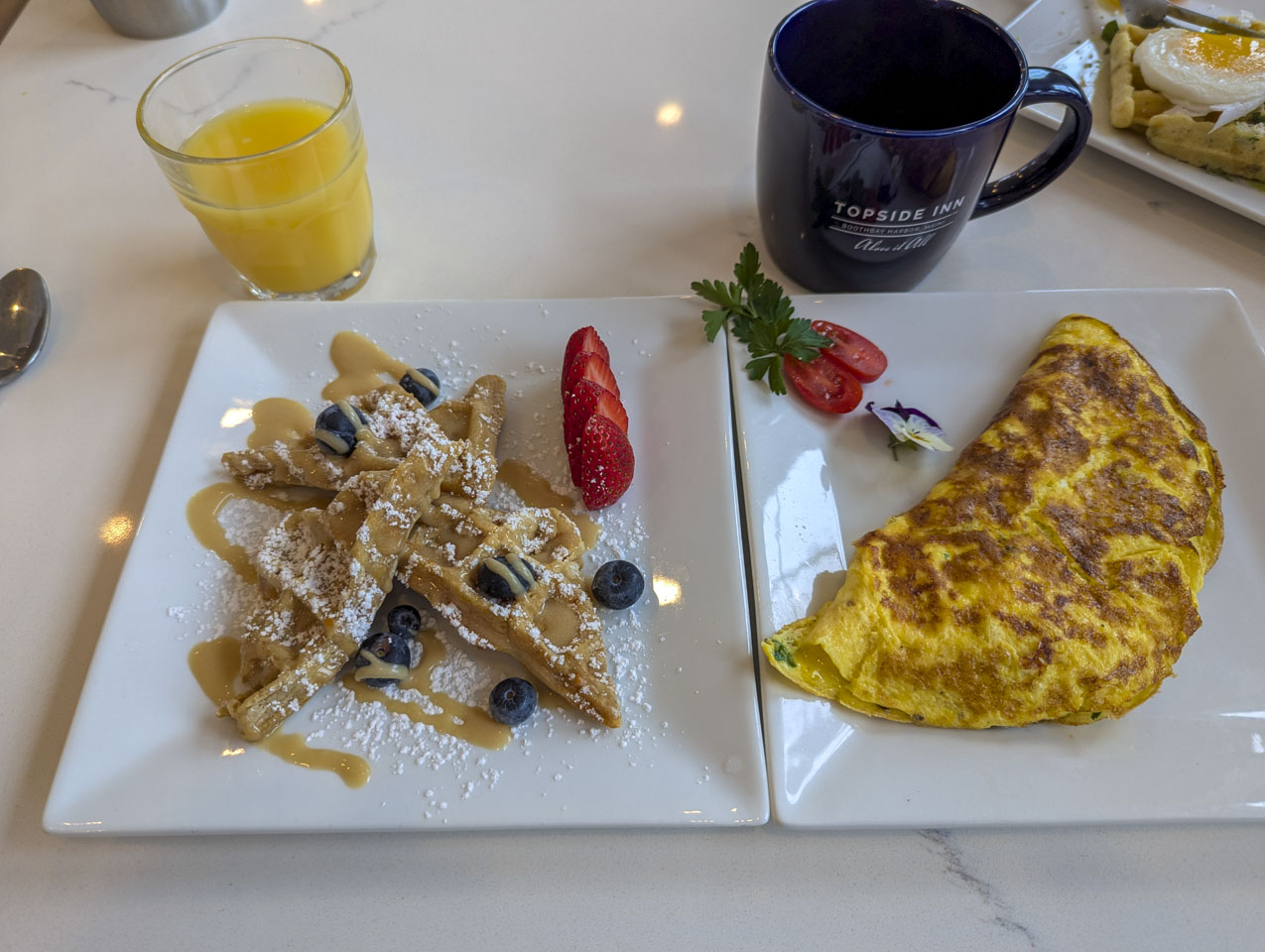 There is a plate with waffles and a plate with omelets for breakfast.