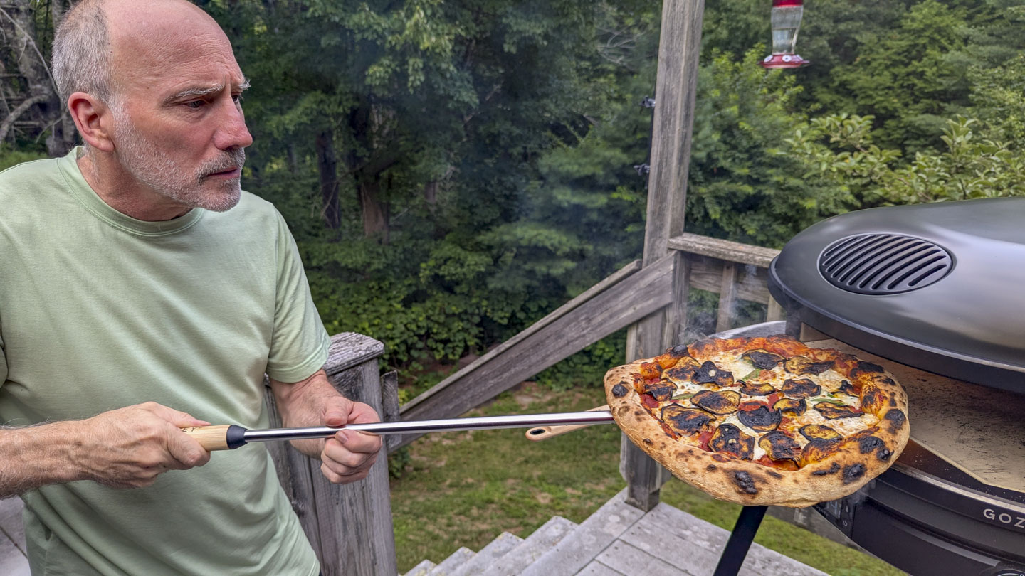 Paul is pulling a pizza out of the pizza oven.