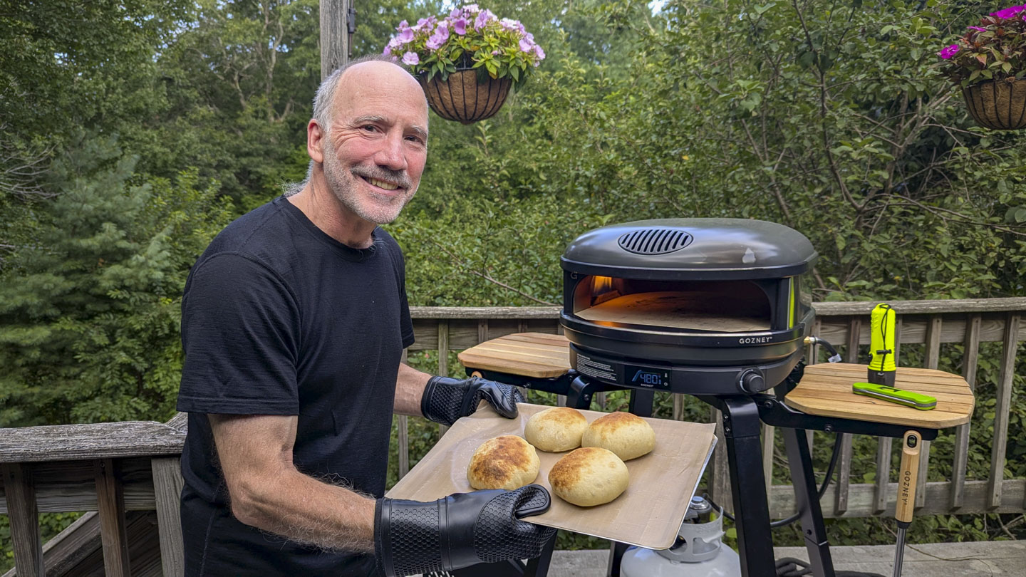 Paul is holding a tray of 4 round rolls that he just pulled out of the pizza oven.