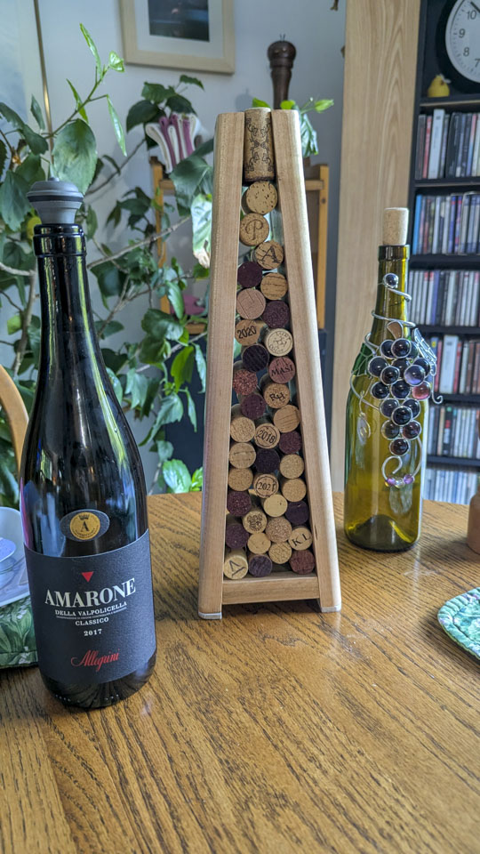 Wine-cork sculpture displayed on a table between a wine bottle and a decorated glass bottle