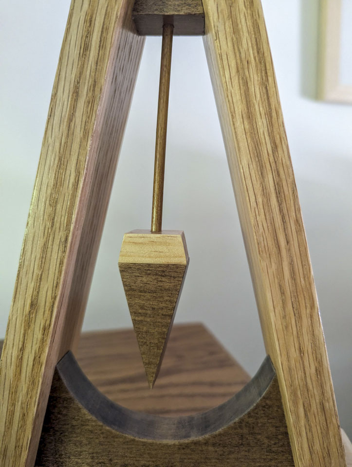 Close-up of the pointed wooden pendulum suspended inside the triangular sculpture