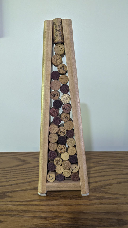 Tall tapered wooden sculpture filled with wine corks in natural and burgundy shades