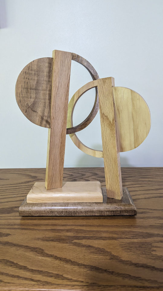 Abstract wooden sculpture made from overlapping circles, semicircles, and upright rectangular pieces