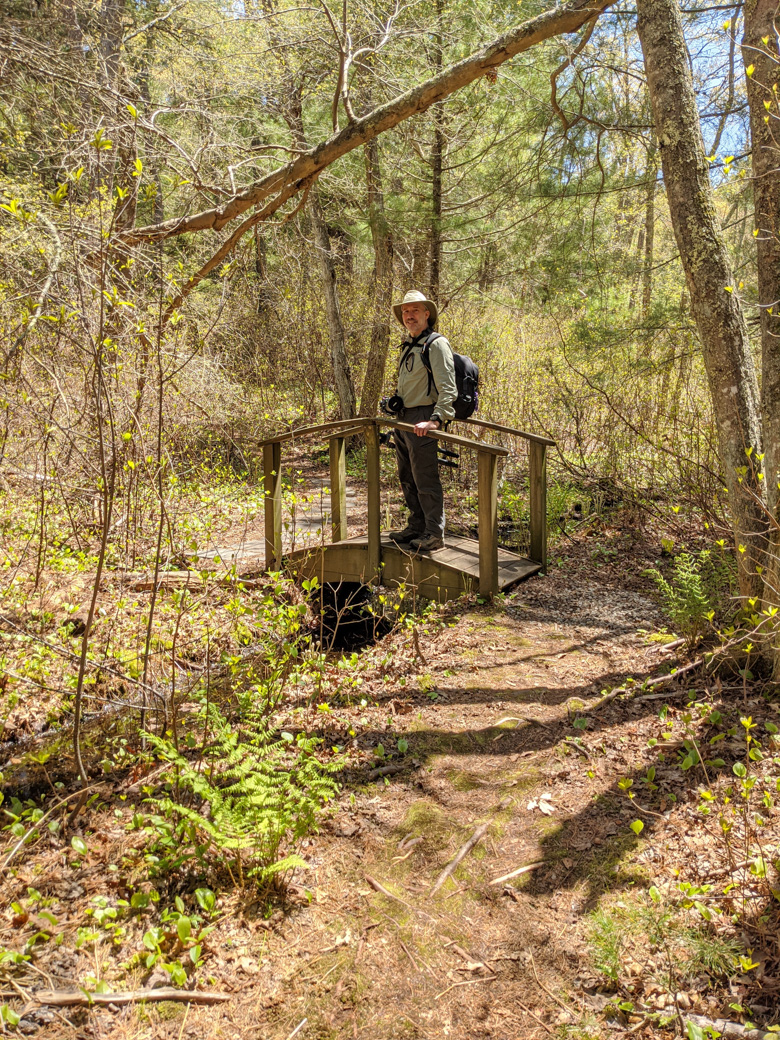 Paul standing on a footbridge in the woods