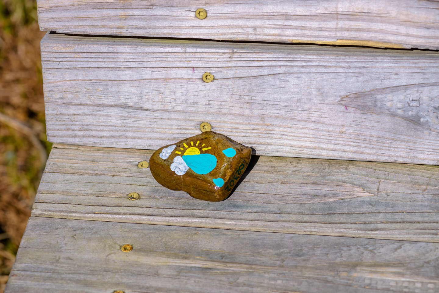 bench with a rock that has sun and clouds painted on it